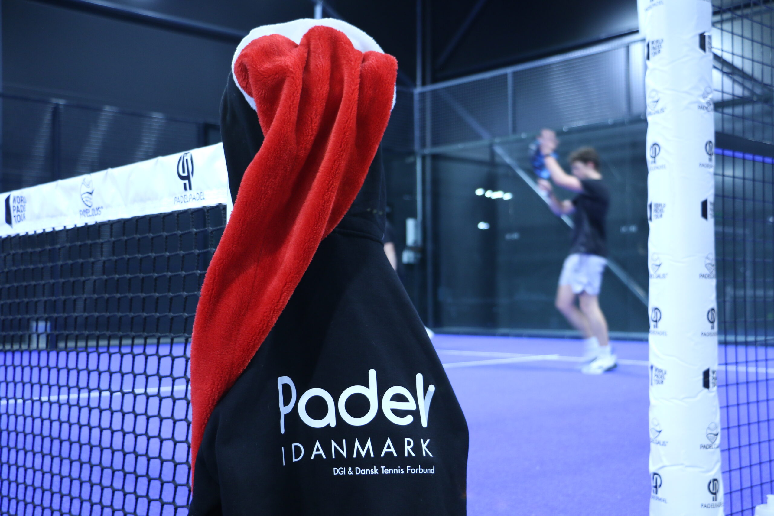 En hættetrøje fra Padel i Danmark hænger på nettet, mens en af deltagerne til dette års julecup anerkender modstanderens spil.